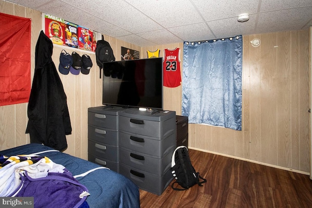 bedroom featuring a paneled ceiling, wooden walls, baseboards, and wood finished floors