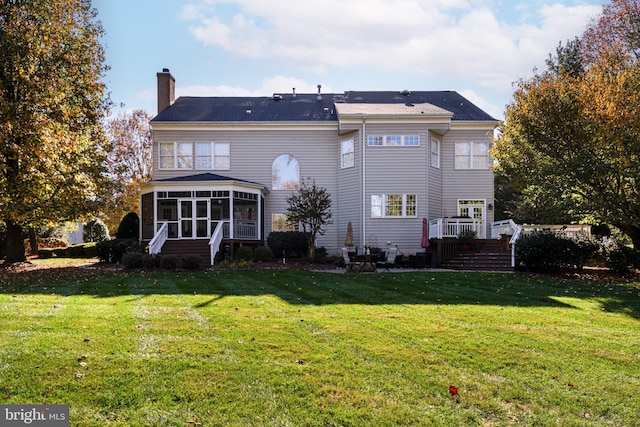 rear view of house with a sunroom, a chimney, and a yard