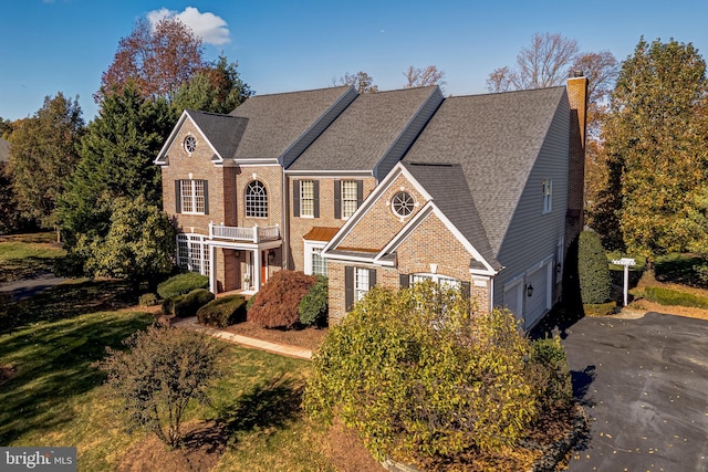 view of front facade with driveway, brick siding, a chimney, and a shingled roof