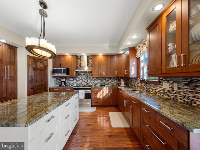 kitchen with a sink, appliances with stainless steel finishes, wall chimney range hood, and glass insert cabinets