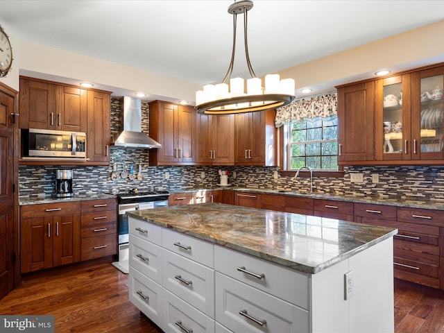 kitchen featuring a center island, glass insert cabinets, stainless steel appliances, wall chimney exhaust hood, and dark wood-type flooring