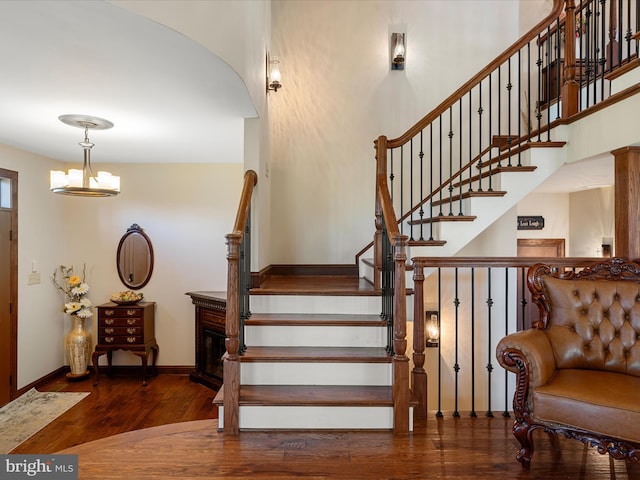 staircase with baseboards, arched walkways, wood finished floors, and a notable chandelier