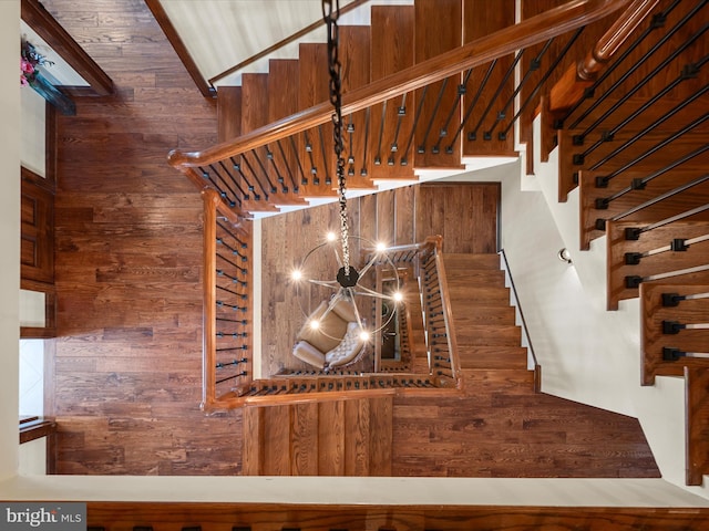 staircase featuring wooden walls and an inviting chandelier