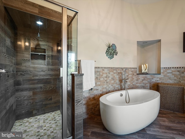 full bathroom with wood finished floors, a freestanding tub, a stall shower, and tile walls