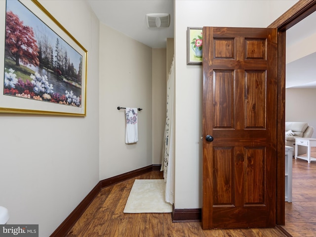 hall featuring baseboards, visible vents, and wood finished floors