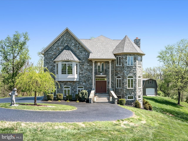 french country home featuring a front yard, a chimney, and stone siding
