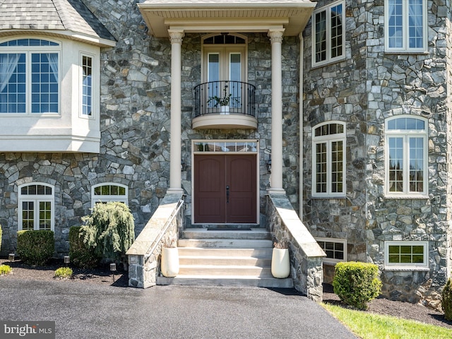 view of exterior entry featuring a balcony and stone siding