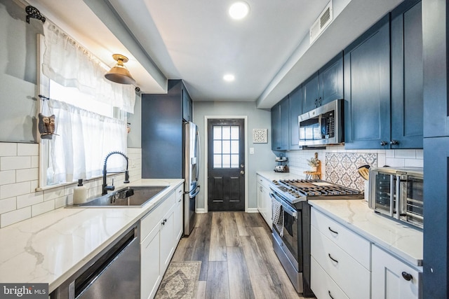 kitchen featuring stainless steel appliances, blue cabinets, sink, light stone counters, and dark wood-type flooring