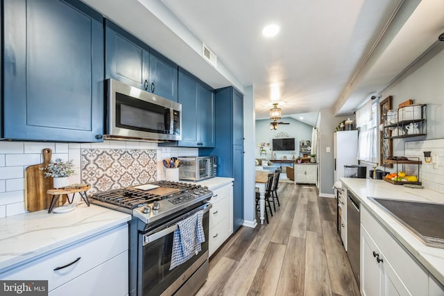 kitchen with light hardwood / wood-style flooring, stainless steel appliances, light stone countertops, blue cabinets, and backsplash