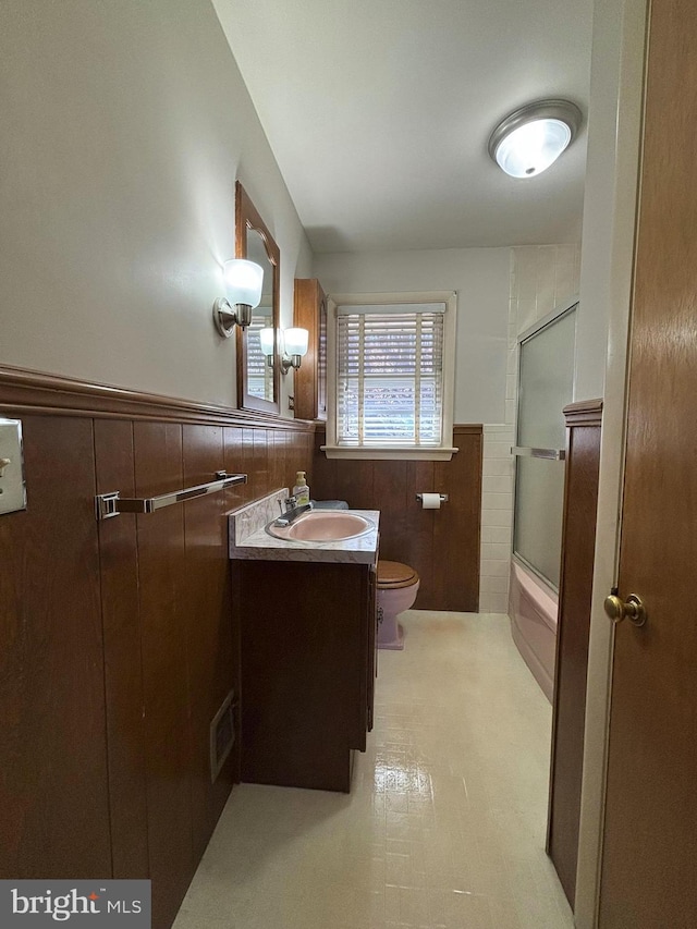 full bathroom with vanity, a wainscoted wall, enclosed tub / shower combo, tile patterned floors, and toilet