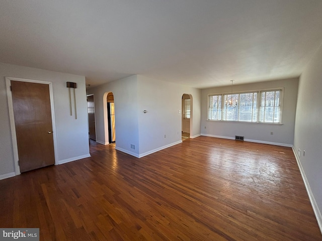 unfurnished living room featuring arched walkways, visible vents, baseboards, and dark wood-style flooring