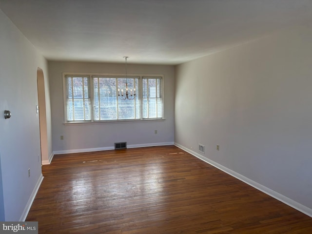 unfurnished dining area featuring dark wood-style floors, baseboards, visible vents, arched walkways, and a notable chandelier