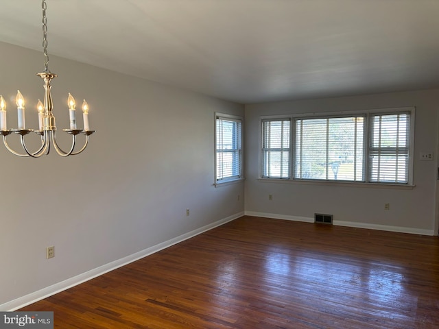 empty room with a healthy amount of sunlight, baseboards, dark wood-type flooring, and an inviting chandelier