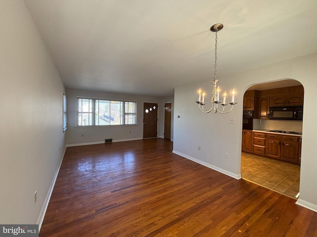 interior space with dark wood-style floors, a chandelier, arched walkways, and baseboards