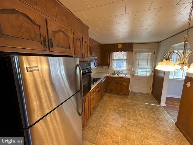 kitchen featuring brown cabinets, a sink, freestanding refrigerator, light countertops, and baseboards