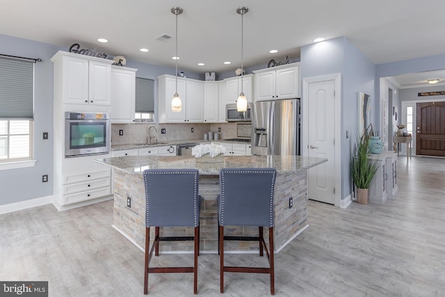 kitchen with a kitchen island, decorative light fixtures, light stone countertops, stainless steel appliances, and white cabinetry