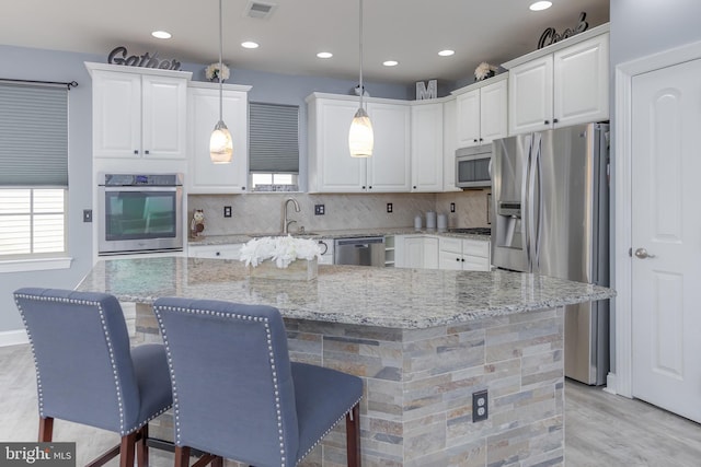 kitchen with appliances with stainless steel finishes, pendant lighting, white cabinets, and a kitchen island