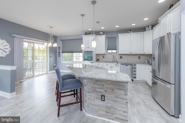 kitchen with white cabinets, light stone countertops, stainless steel appliances, and a center island