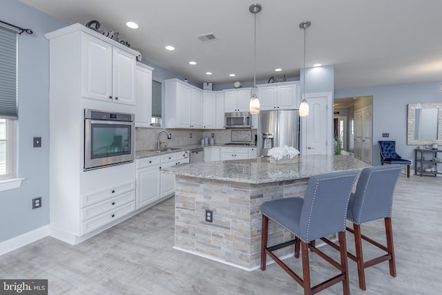 kitchen featuring light stone counters, appliances with stainless steel finishes, white cabinetry, and a center island