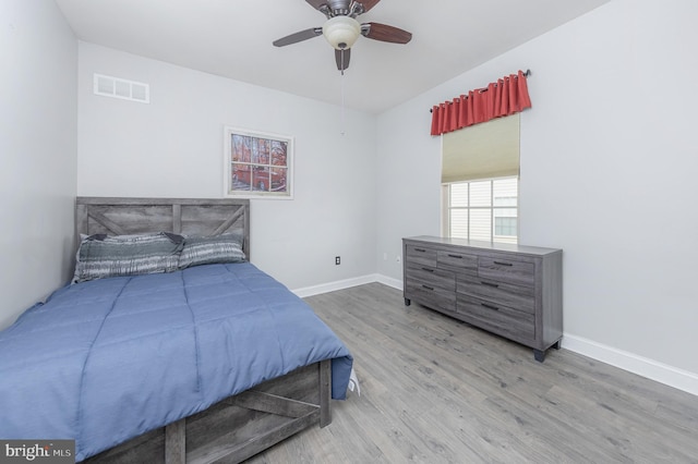 bedroom with a ceiling fan, visible vents, baseboards, and wood finished floors