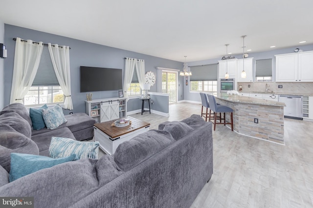 living room featuring a chandelier, baseboards, light wood-style flooring, and a healthy amount of sunlight