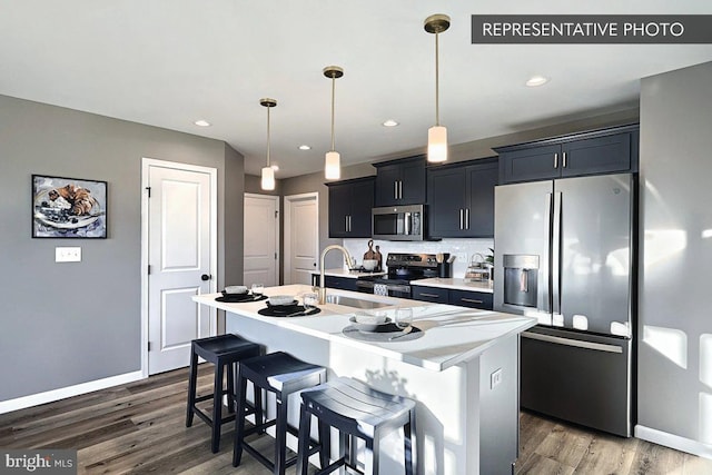 kitchen with appliances with stainless steel finishes, a center island with sink, decorative light fixtures, a breakfast bar, and sink