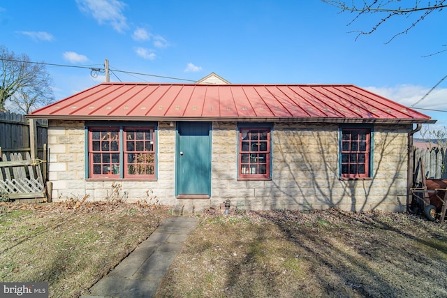 bungalow-style home featuring metal roof, stone siding, a standing seam roof, and fence