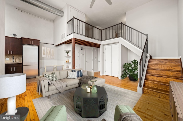 living room featuring a towering ceiling, ceiling fan, and light hardwood / wood-style flooring