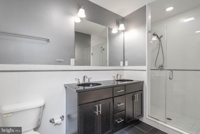 bathroom with a shower with door, tile patterned floors, toilet, tile walls, and vanity