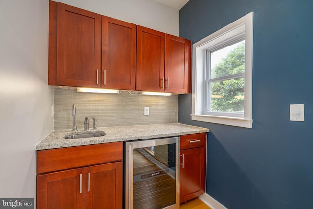 bar featuring decorative backsplash, sink, light stone countertops, and beverage cooler