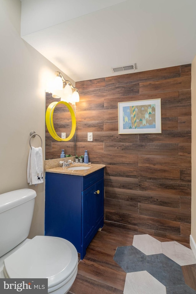 bathroom featuring hardwood / wood-style floors, toilet, wooden walls, and vanity