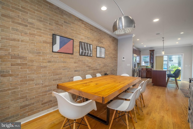 dining space featuring brick wall, ornamental molding, and light hardwood / wood-style floors