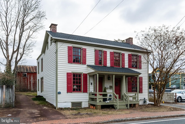 view of front facade featuring a porch, roof with shingles, and a chimney