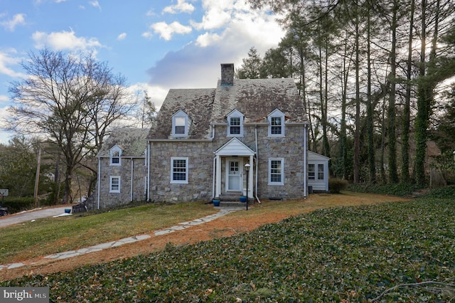 view of front of home featuring a front yard, stone siding, and a chimney