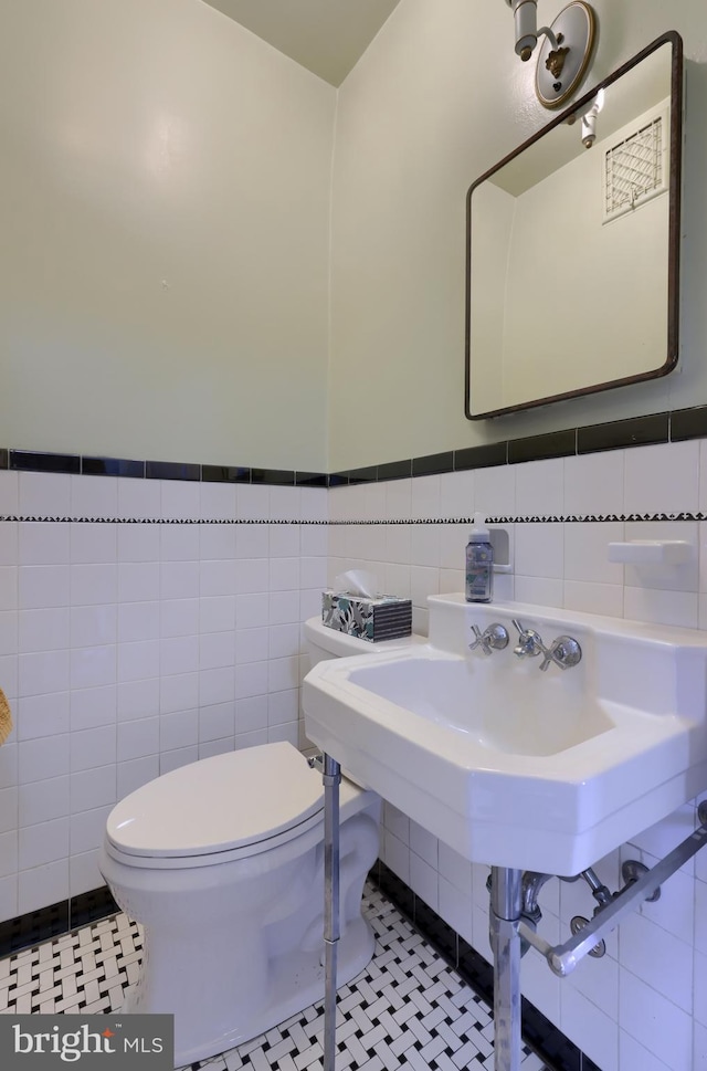 half bath with toilet, tile walls, and tile patterned floors