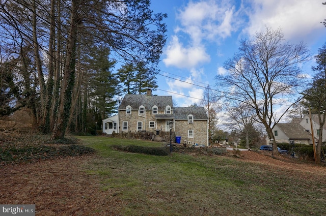 view of front facade with a chimney, a front yard, and stone siding