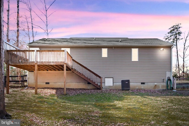 back house at dusk with central air condition unit, a deck, and a yard