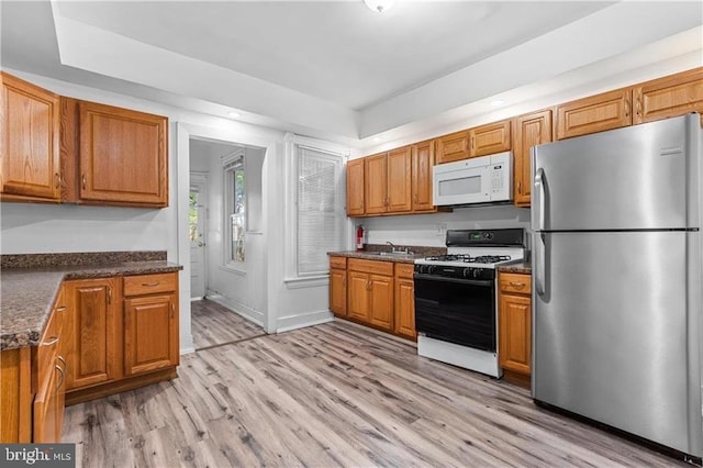 kitchen featuring brown cabinetry, white microwave, freestanding refrigerator, light wood-type flooring, and gas stove