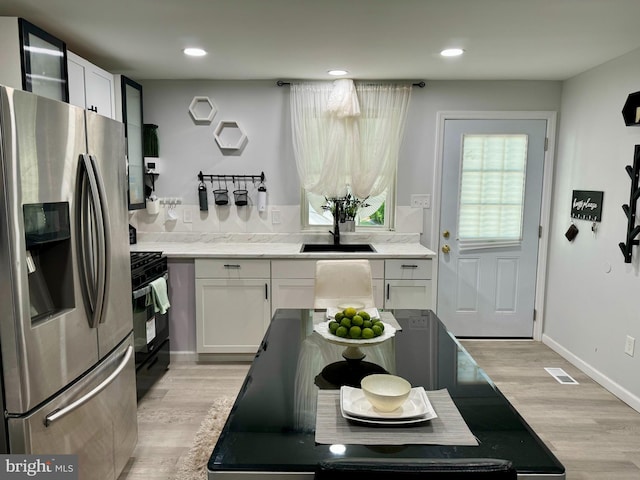 kitchen with light wood-type flooring, gas stove, stainless steel refrigerator with ice dispenser, sink, and white cabinets