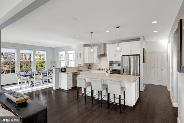 kitchen with dark wood-style floors, appliances with stainless steel finishes, a peninsula, wall chimney range hood, and a sink