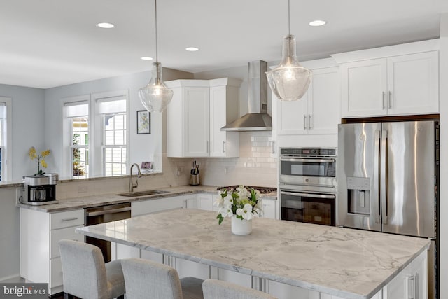 kitchen featuring stainless steel appliances, backsplash, a sink, a peninsula, and wall chimney exhaust hood