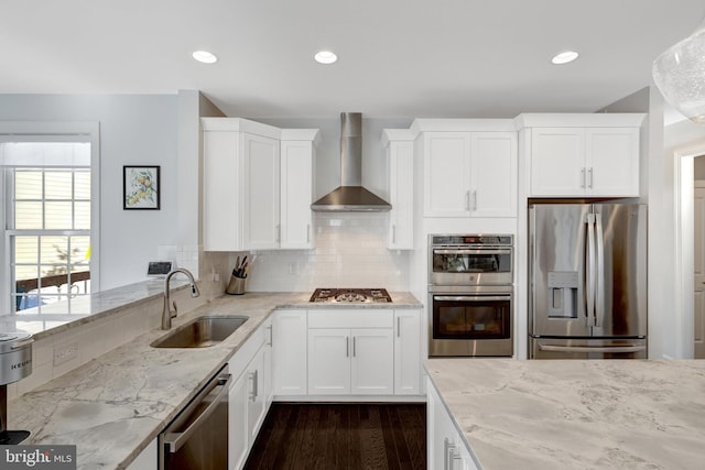 kitchen with stainless steel appliances, a sink, white cabinets, wall chimney range hood, and light stone countertops