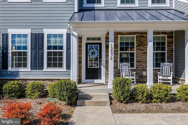 doorway to property featuring covered porch, stone siding, a standing seam roof, and metal roof