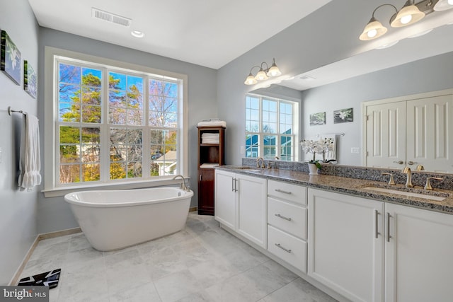 bathroom with double vanity, a soaking tub, visible vents, and a sink