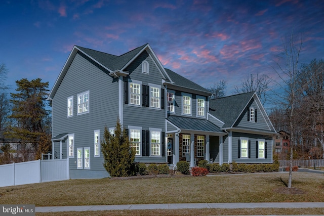 view of front facade with a yard, a shingled roof, a standing seam roof, fence, and metal roof