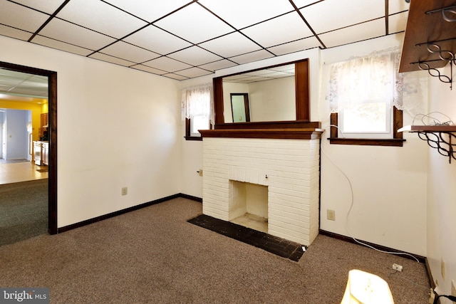 unfurnished living room featuring a brick fireplace, dark carpet, and a drop ceiling