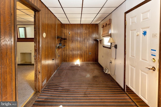 corridor featuring wooden walls, dark colored carpet, and a drop ceiling