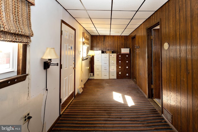 hall with dark carpet, a paneled ceiling, and wooden walls