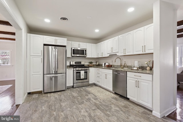 kitchen with appliances with stainless steel finishes, light hardwood / wood-style flooring, white cabinets, stone counters, and sink