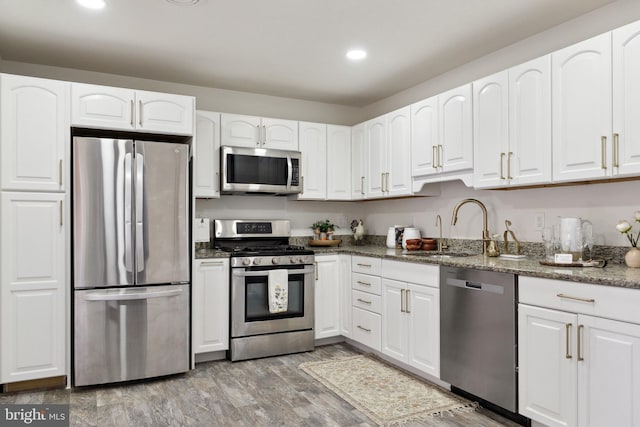 kitchen featuring appliances with stainless steel finishes, wood-type flooring, sink, white cabinetry, and dark stone countertops